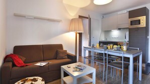A compact living space with a sofa, a small table, a dining area with chairs, a kitchen with a microwave, and a lamp. - Spacious Alpine Retreat for Groups (Les Deux Alpes)