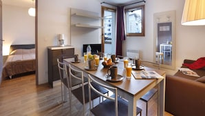 A compact hotel room with a kitchenette, a dining area with a table and chairs, a bed, and a large window. - Spacious Alpine Retreat for Groups (Les Deux Alpes)