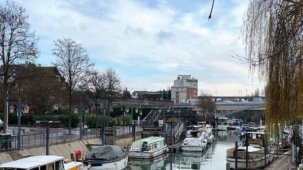 A canal with boats docked, a bridge in the background, and buildings along the riverbank. - Spacious Alpine Retreat for Groups (Les Deux Alpes)