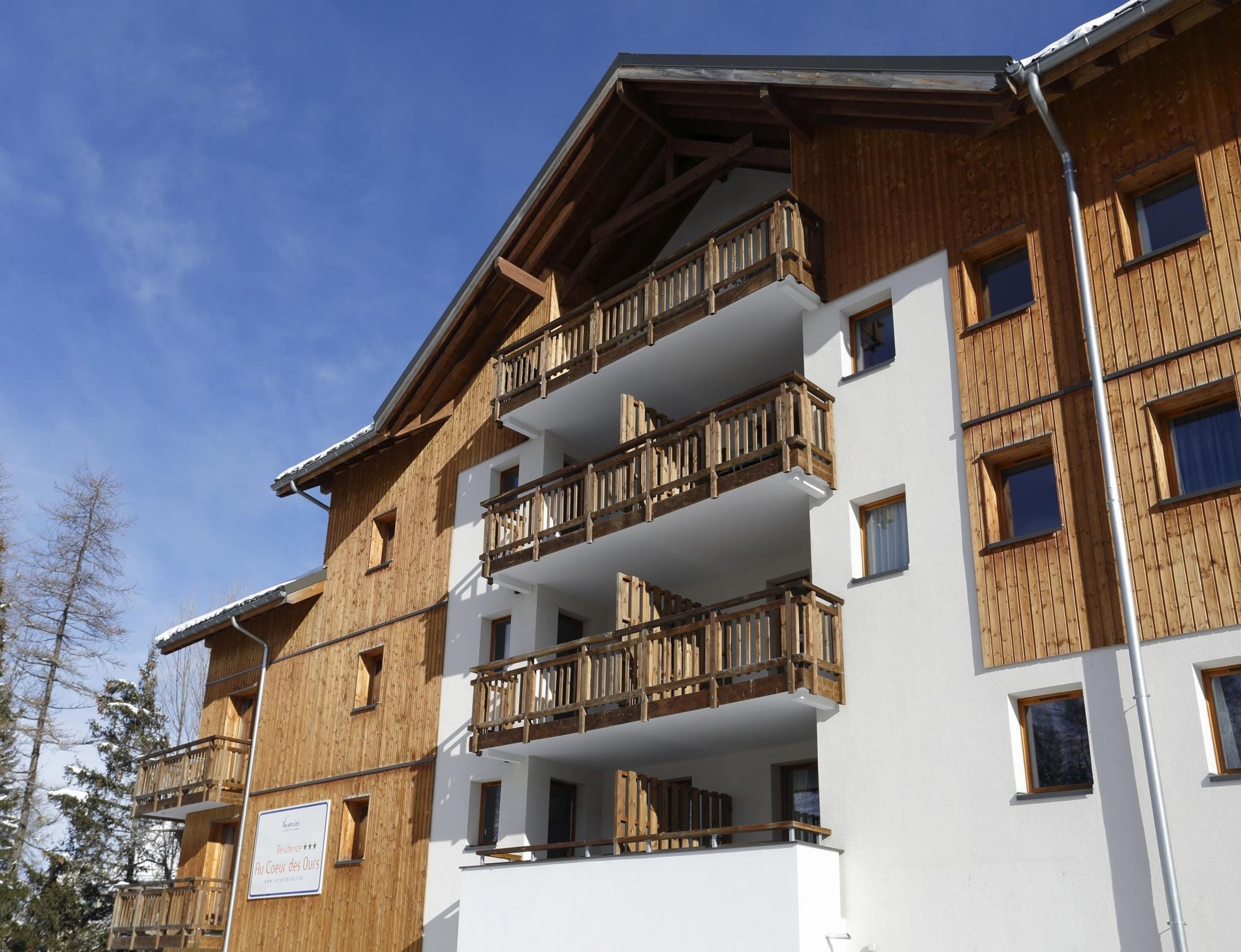 Un edificio de varios pisos con balcones de madera y paredes blancas, que presenta un letrero con texto.