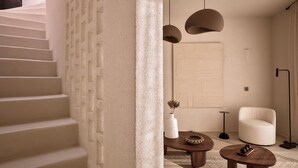 A modern interior with a staircase, a round wooden table, a white armchair, and pendant lighting.
