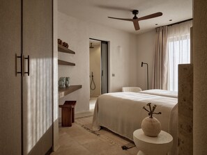 A bedroom with a bed, a bedside table, a nightstand, a ceiling fan, a window with curtains, and a door leading to another room.