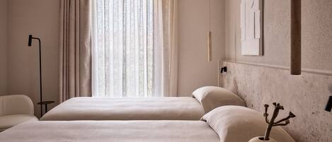 A hotel room with two beds, a large window with curtains, a floor lamp, and a vase with branches on a side table.