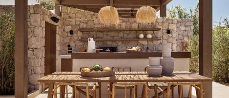 An outdoor dining area with a stone wall, wooden pergola, and woven chairs.
