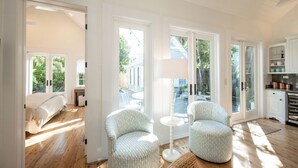 Een lichte kamer met een bed, twee stoelen, een lamp en een keukenhoek met kasten.