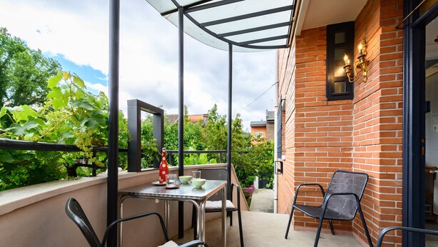 Ein Balkon mit Tisch, Stühlen, einer Glastür und einer Ziegelwand.