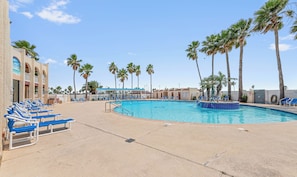 A pool area with blue lounge chairs, palm trees, and a building with arched windows.