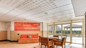 Um lobby de hotel com uma receção, uma área de estar com sofá e cadeiras, e uma janela ampla que oferece vista para o exterior.