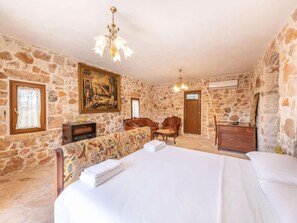 A room with stone walls, a bed, a sofa, a chair, a painting, and a chandelier. - Villa Pietra D'ulivo (Ceglie Messapica)