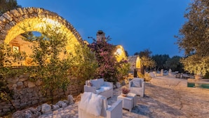 Un espacio al aire libre con paredes y arcos de piedra, rodeado de vegetación y suelo de piedra.