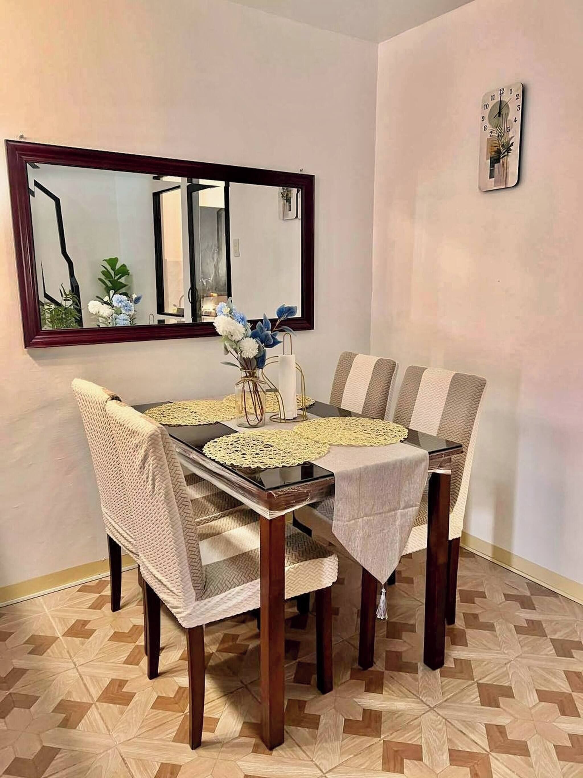 Un comedor con una mesa, sillas, un espejo y un reloj en la pared.