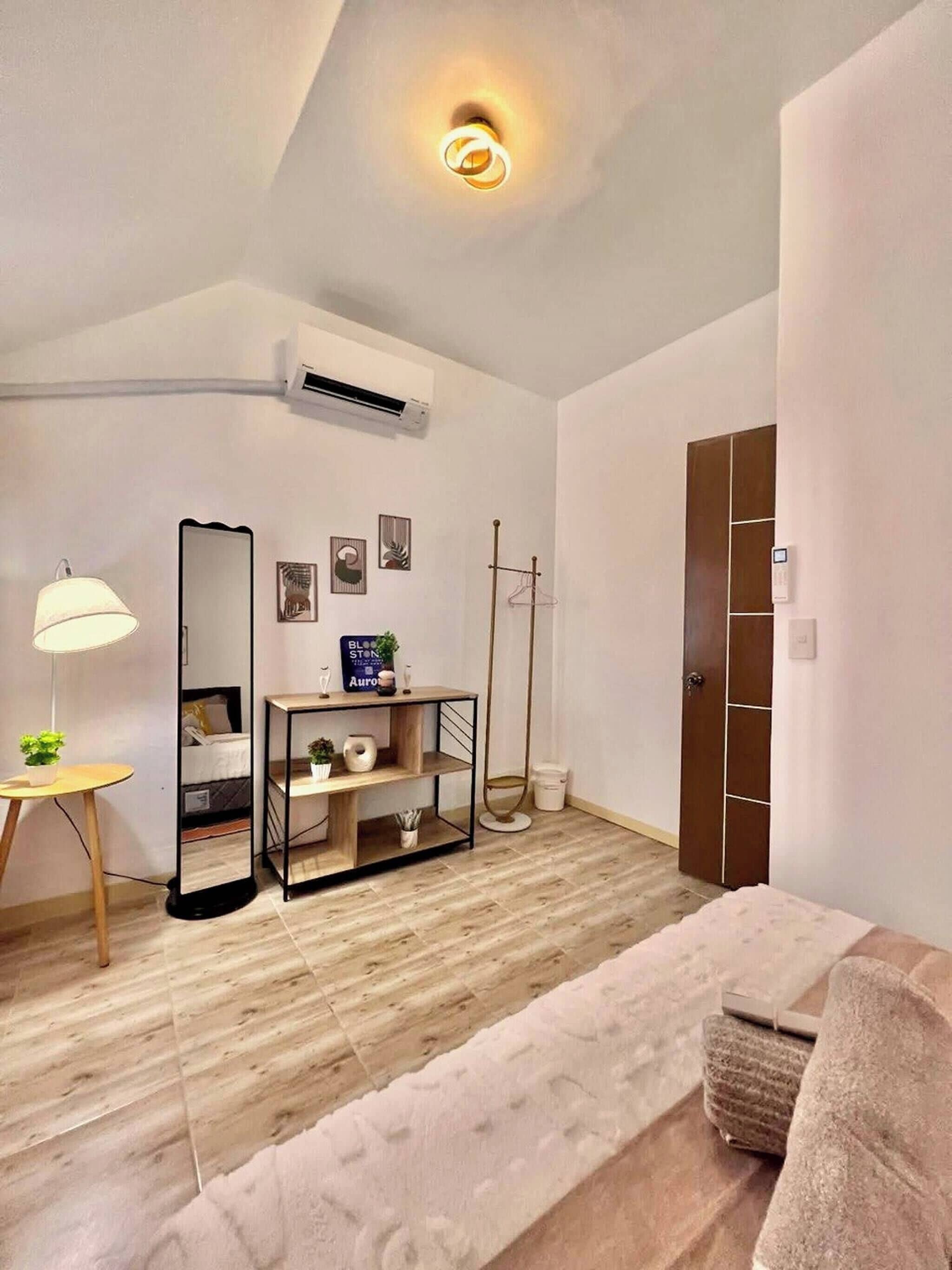Una habitación moderna con suelo de madera, un espejo, una lámpara, una mesita con una planta y un armario.