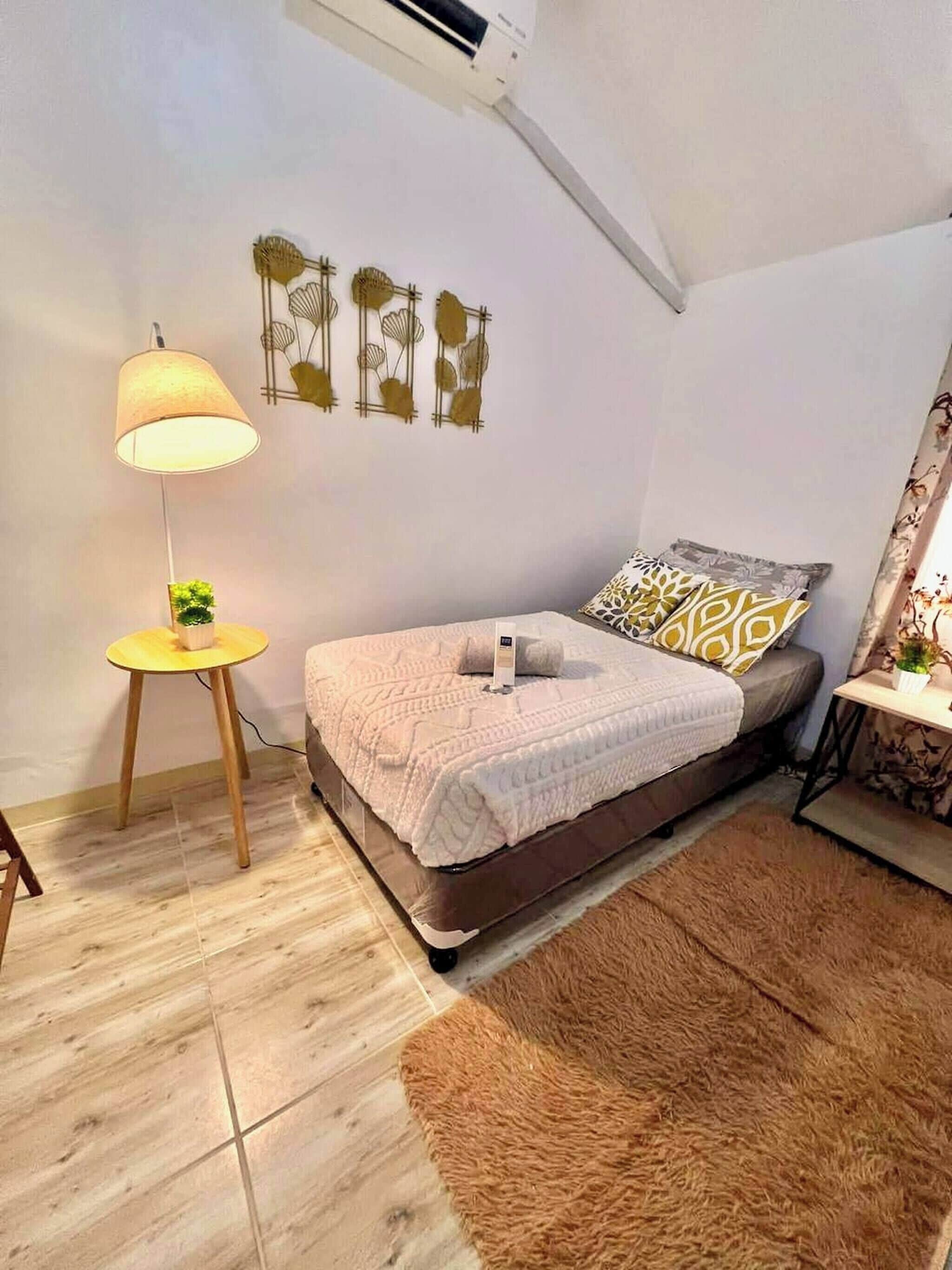 Een slaapkamer met een bed, een lamp, een tafeltje met een plant en wanddecoratie.