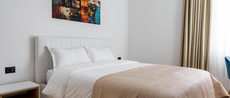Una habitación de hotel moderna con una cama blanca, una mesita de noche pequeña y un cuadro abstracto colorido en la pared.