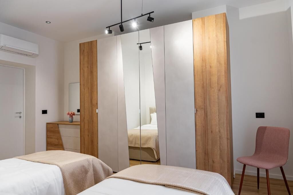 Une chambre avec deux lits, une armoire en bois, un miroir et une chaise rose.