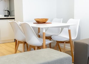 Uma área de refeições com uma mesa branca, quatro cadeiras brancas e uma tigela de madeira sobre a mesa.