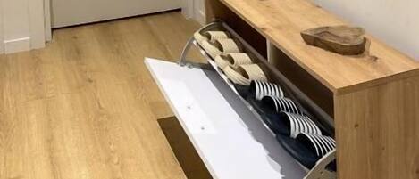 A hallway with a wooden cabinet, a mirror, and a shoe rack.