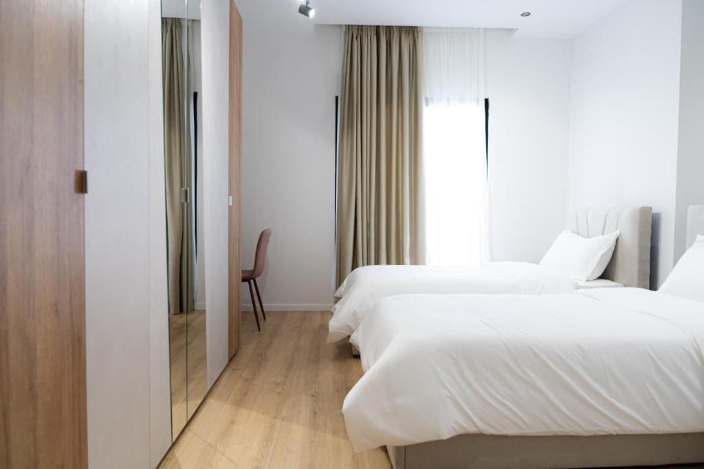 Ein Hotelzimmer mit Holzboden, einem Bett mit weißer Bettwäsche, einem Sessel und einem Fenster mit Vorhängen.