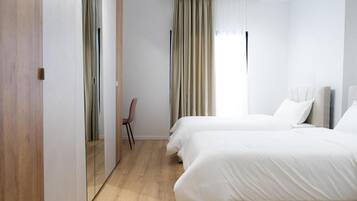 Ein Hotelzimmer mit Holzboden, einem Bett mit weißer Bettwäsche, einem Sessel und einem Fenster mit Vorhängen.