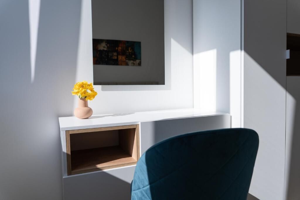 A room with a white console table, a painting, and a vase with yellow flowers.