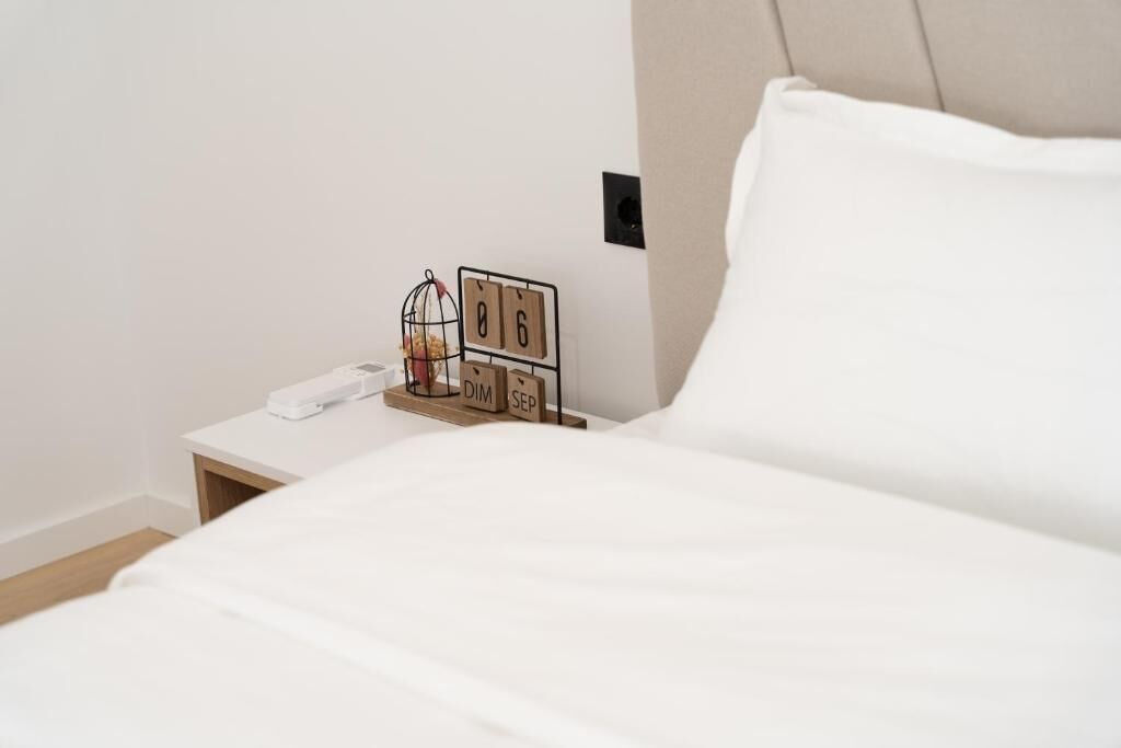 Un lit bien fait, avec une literie blanche, une table de chevet sur laquelle se trouve un téléphone blanc et un objet décoratif, et un calendrier mural affichant le mois de septembre.