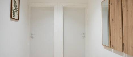 Una habitación con dos puertas blancas, un mueble de madera con un espejo y una pequeña planta sobre una consola de madera.