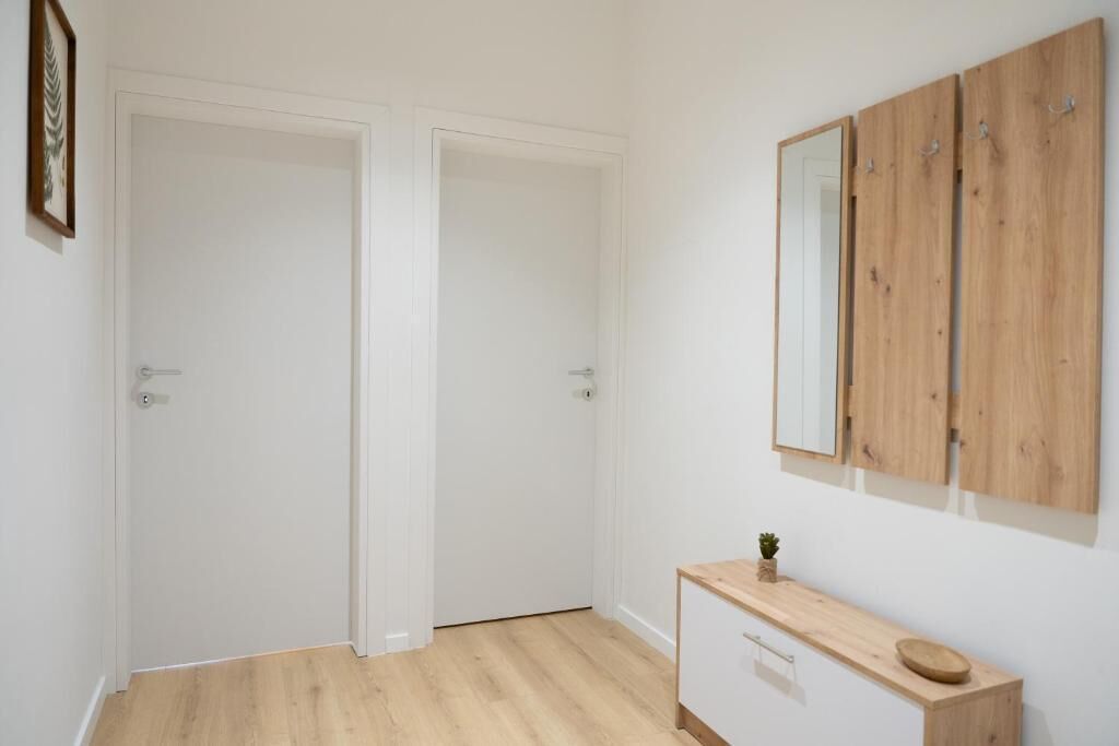A room with a wooden floor, white walls, a wooden vanity with a mirror, and two white doors.
