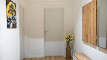 Un couloir avec une porte blanche, un banc en bois, un vase de fleurs et un tableau accroché au mur.