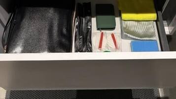 Ett handfat på hotellrummets badrum, med en spegel ovanför, en handduksställning och en förvaringslåda under som innehåller toalettartiklar och en svart väska.