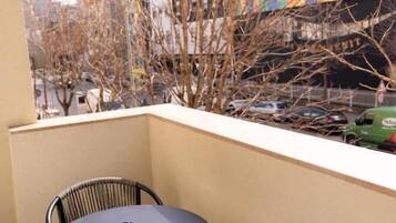 A balcony with a round table and two chairs, overlooking a street with buildings and parked cars.