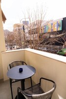 A balcony with a round table and two chairs, overlooking a street with buildings and parked cars.
