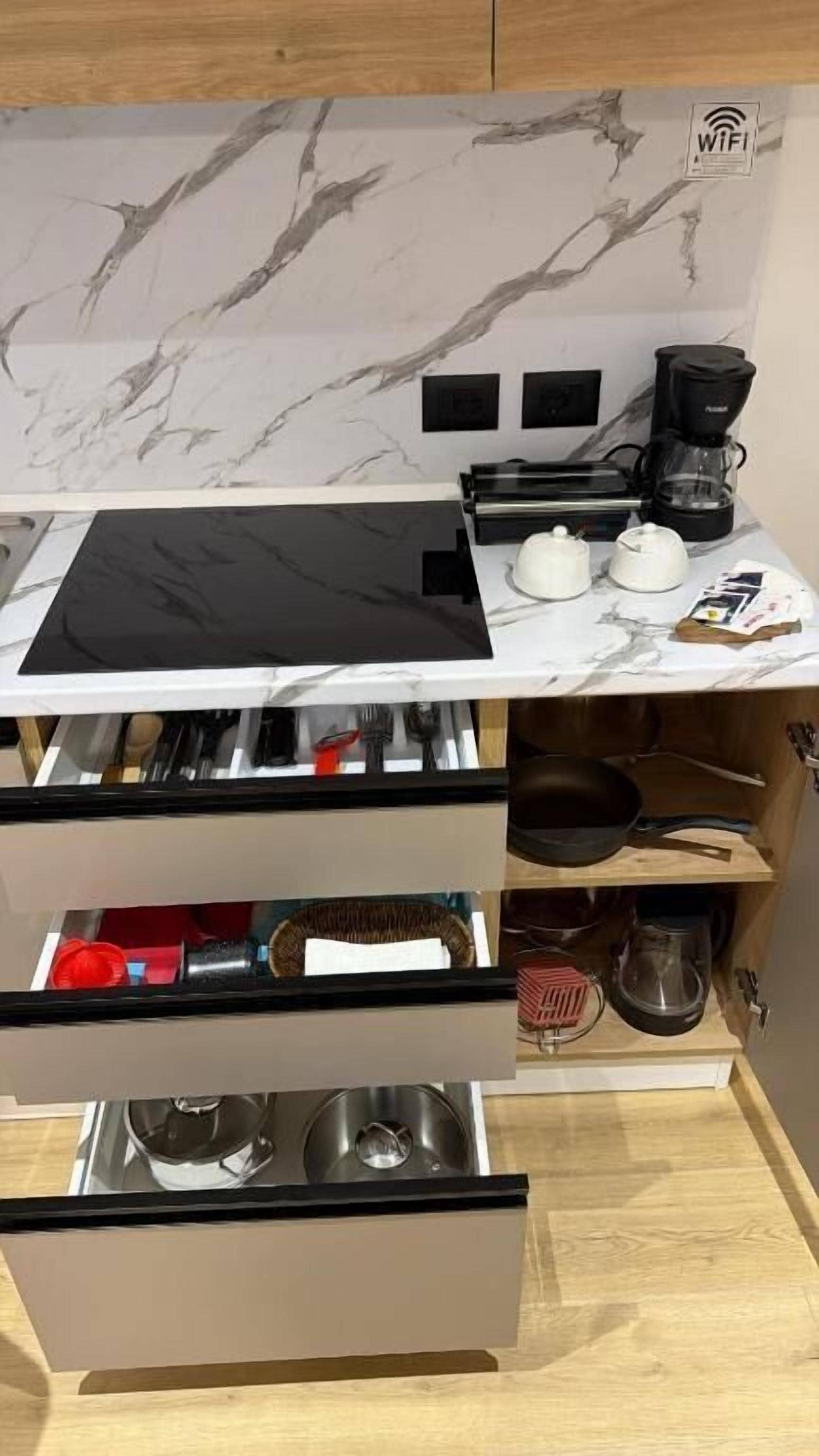 A kitchen with a marble backsplash, a black countertop, and a built-in drawer with utensils.