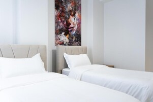 A hotel room with two beds, a large abstract painting on the wall, and a window with sheer curtains.