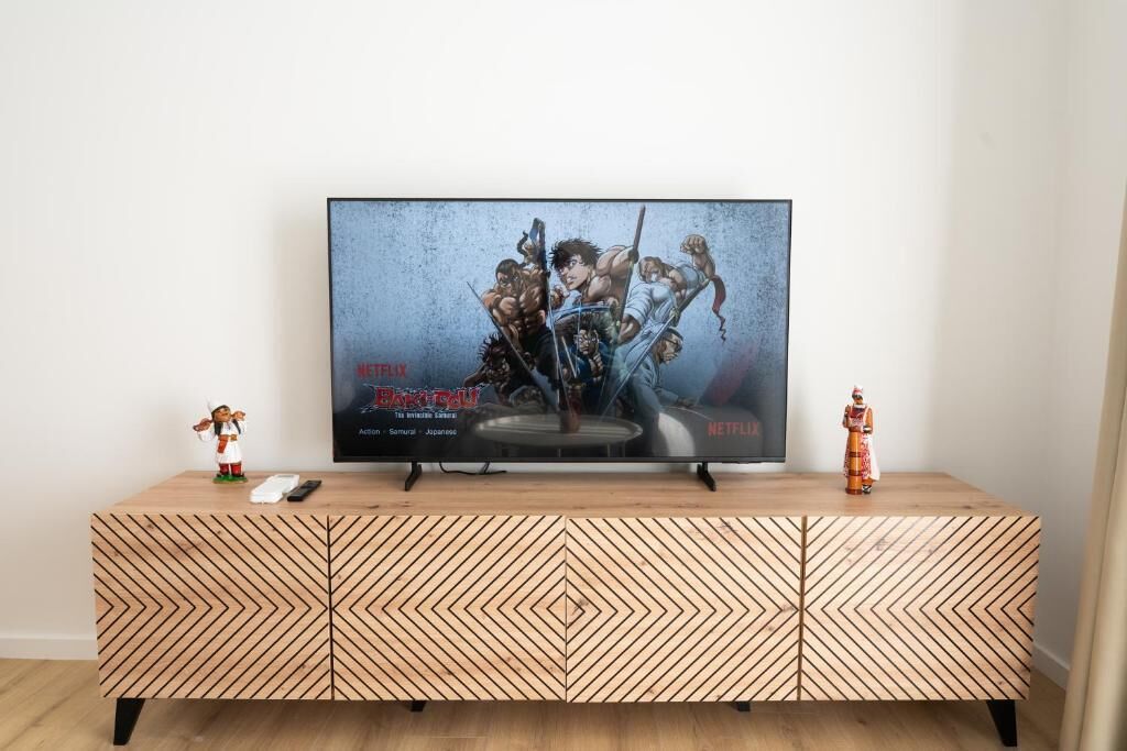 Un téléviseur posé sur un meuble en bois orné d’un motif géométrique, une télécommande et deux figurines sur le dessus du meuble.
