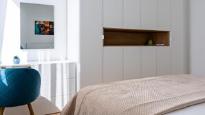A bedroom with a bed, a blue chair, a small shelf with a plant, and a wall-mounted picture. - Barrikada - E Apartments (Tirana)