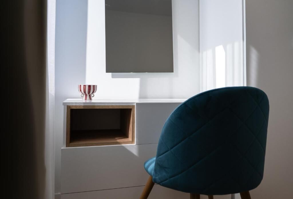 A room with a window, a blue chair, and a small wooden shelf with a red and white striped object.