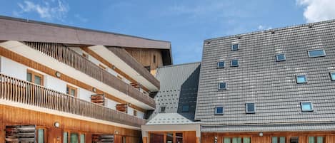 Ein modernes Gebäude mit Holzfassade und Flachdach, ein Innenhof mit Pongtisch und ein Gebäude mit Ziegeldeckung.