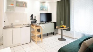 A compact hotel room with a kitchenette, a bed, a small table with fruit, and a TV. - Mega Cool apartment between France and Switzerland - near Basel (Saint-Louis)