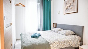 A bedroom with a bed, a hanging wooden hanger, a teal curtain, and a framed floral artwork on the wall. - Mega Cool apartment between France and Switzerland - near Basel (Saint-Louis)