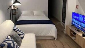 Una habitación de hotel moderna con cama, sofá, televisor y lámpara.