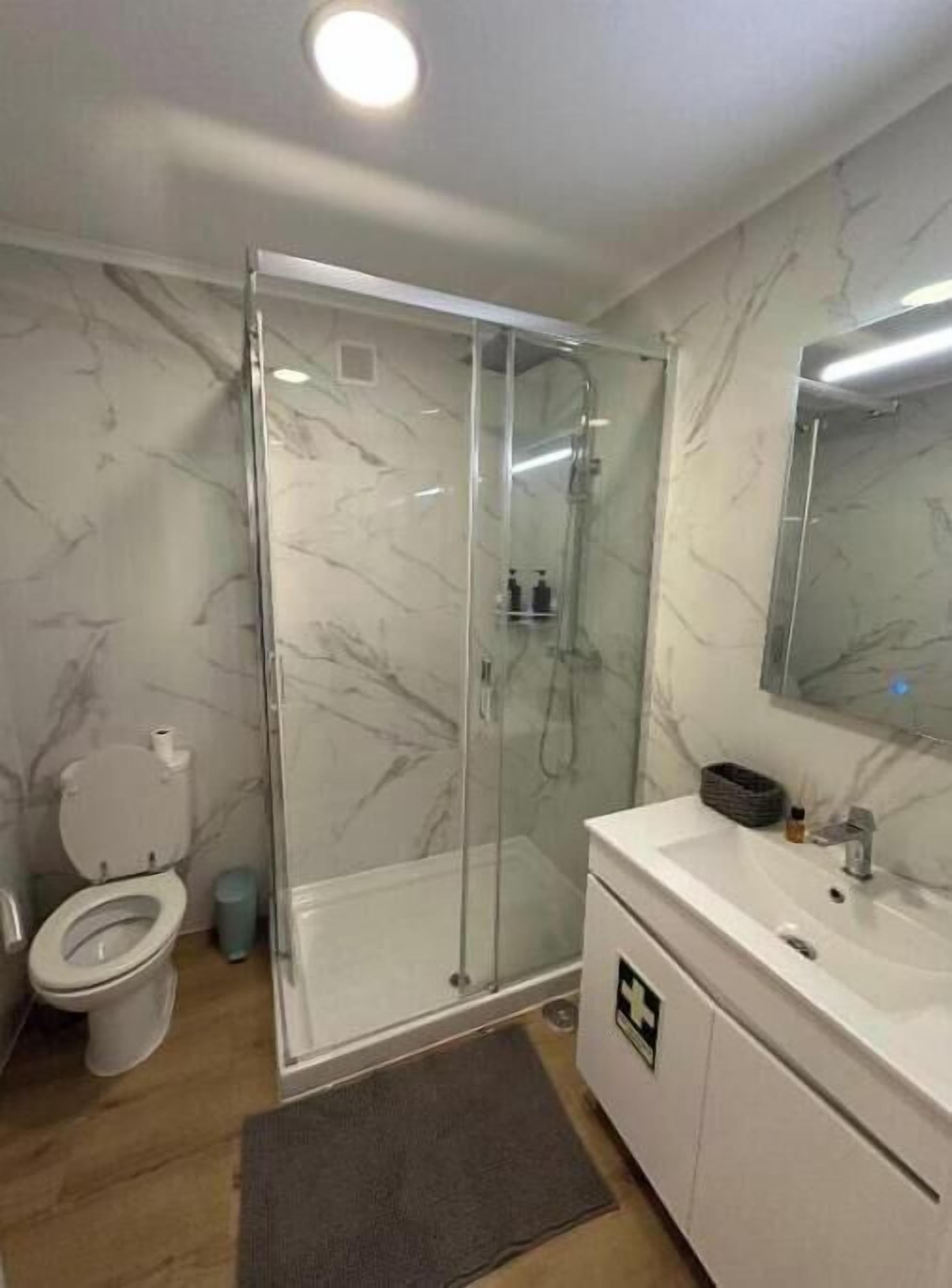 Ein Badezimmer mit Duschkabine, Toilette, Waschbecken mit Spiegel und Marmorwänden.