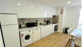 Una cocina compacta con muebles blancos, lavadora y comedor con mesa y sillas.
