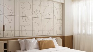 Hotellihuone, jossa on sänky, yöpöytä, abstraktilla kuviolla koristeltu seinä ja läpikuultavat verhot.