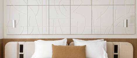 A hotel room with a bed, two bedside tables, a headboard, and a wall with abstract line art.