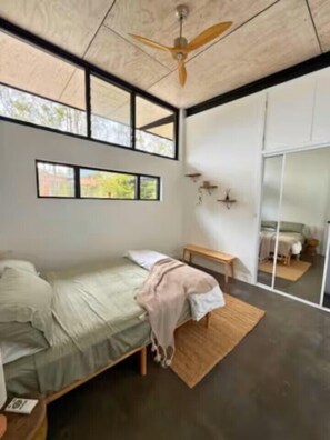 A modern bedroom with a bed, a bench, a ceiling fan, and a large window.