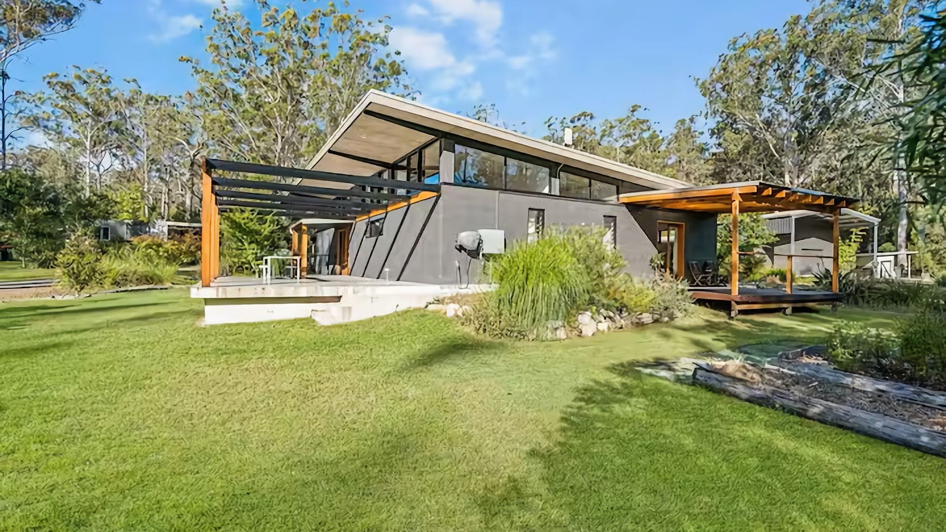 Una casa moderna con una terraza amplia, un espacio de estar techado al aire libre y un césped cuidado.