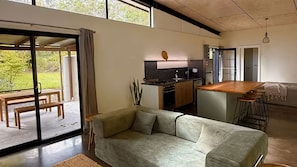 A modern interior with a sofa, a dining area, a kitchen, and a sliding glass door leading to an outdoor space.