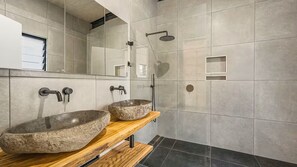 A modern bathroom with two stone sinks, a shower, and a mirror.