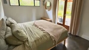 A bedroom with a bed, pillows, a nightstand, a mirror, and a view through a glass door.