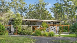A modern house with a large glass facade, surrounded by lush greenery and trees. - Teague Retreat Studio Space (South Kempsey)